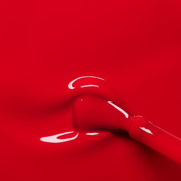 A close-up of Manucurist’s Poppy Red gel polish being applied, revealing a smooth, shiny layer of vibrant red color spreading evenly across the nail.