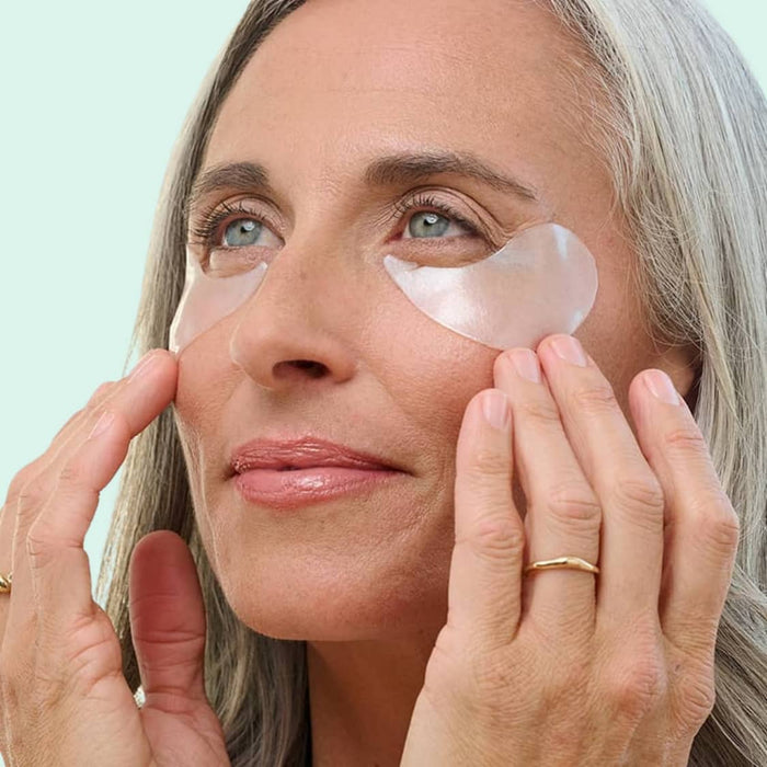 Woman applying patches under her eyes with a light green background