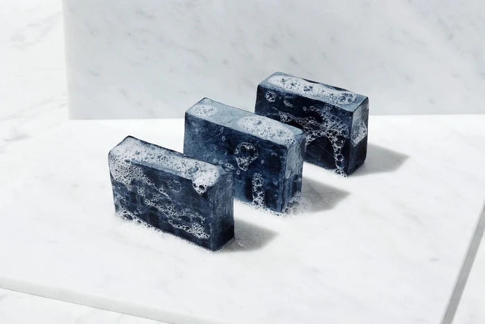 three black artisan soap bars with white lather on marble surface
