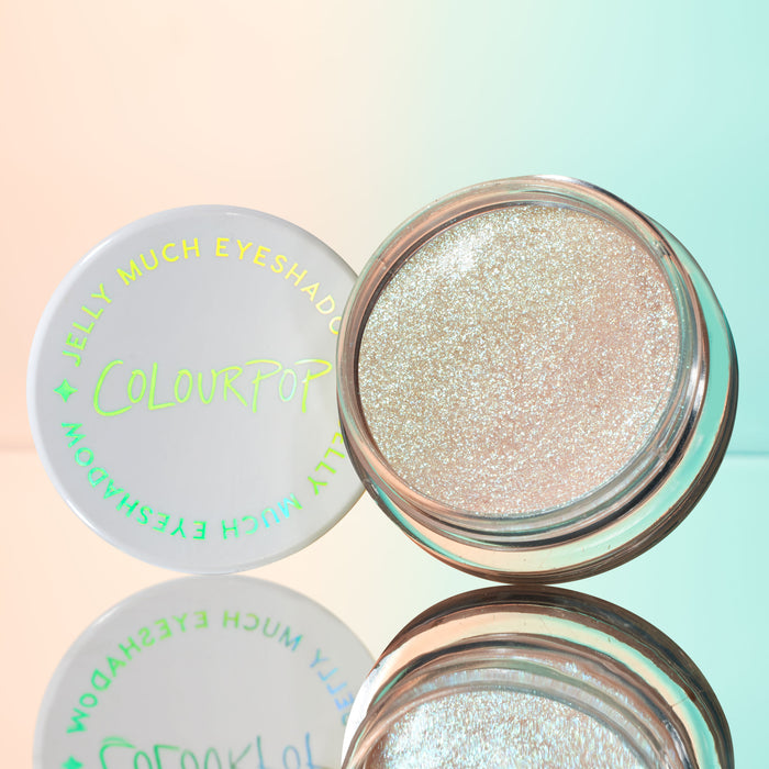 Open pot of ColourPop Jelly Much Shadow in Sage Bundle, a sparkling icy-champagne gel eyeshadow, sits beside its white lid with iridescent logo on a mirrored surface against a pastel peach-to-mint gradient.