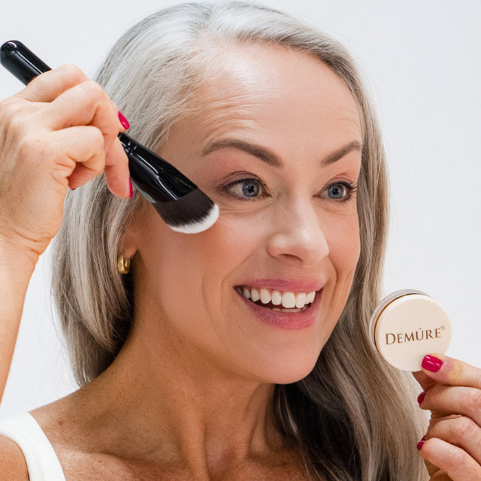 A woman apply blush with a Sculpting Contour Brush  and holding a makeup jar in her other hand.