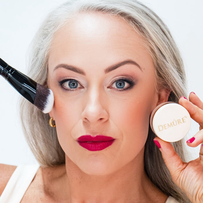 A woman apply blush with a Sculpting Contour Brush  and holding a makeup jar in her other hand.