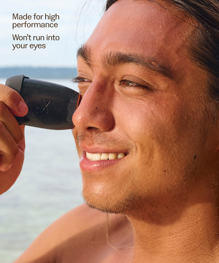 Man smiling while applying Signature SPF 50 Tinted Mineral Face Stick by Sun Bum near his eye outdoors