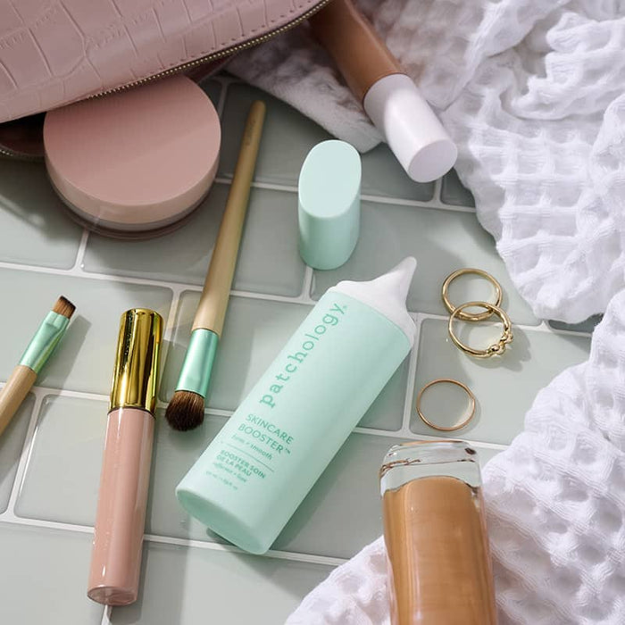 Patchology Skincare Booster mint bottle with makeup brushes and cosmetics, flat lay beauty routine setup on tiled surface