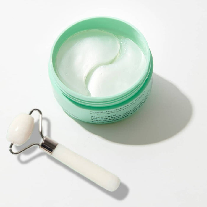 Jar of hydrogel under-eye patches with curved white gels inside, paired with a facial roller tool, showcasing soothing and depuffing skincare essentials