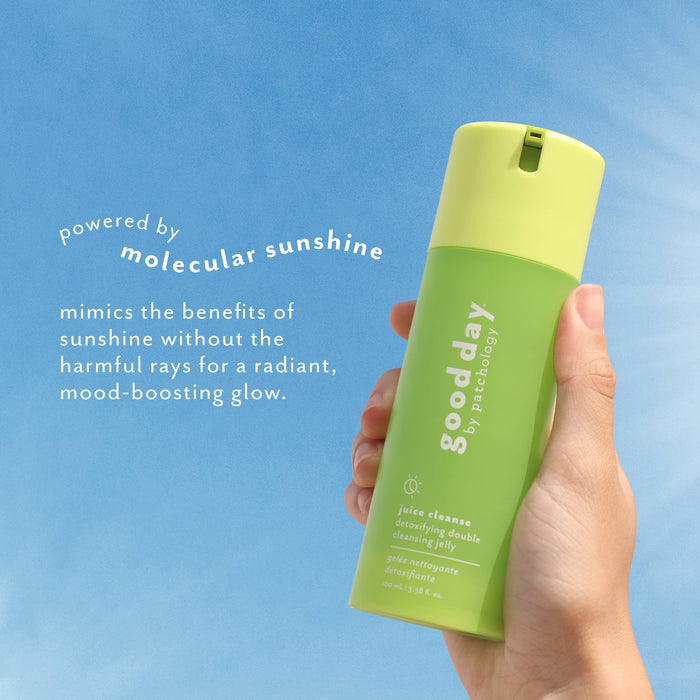 A hand holding a green and yellow bottle ofJuice Cleanser against a blue sky background with white descriptive text.