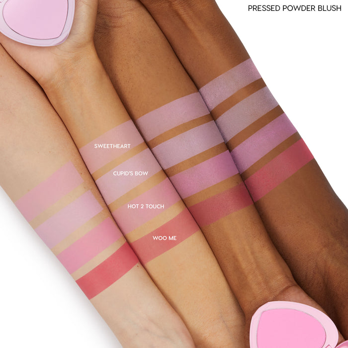 ColourPop Pressed Powder Blush in Sweetheart swatched as a soft matte pink stripe across three arms in light, medium, and deep skin tones, shown alongside Cupid’s Bow, Hot 2 Touch, and Woo Me for comparison, with a pink heart compact at the edges.