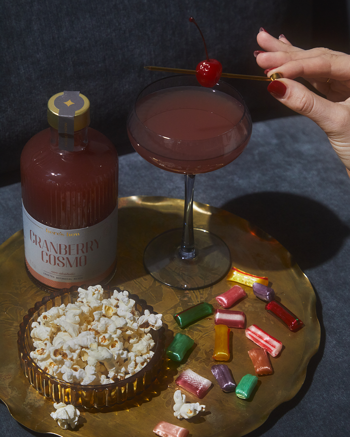 Gold cocktail pick held above a cocktail glass with a red cherry