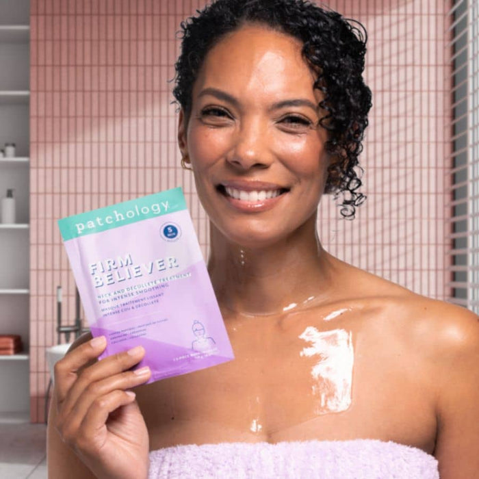 Woman with glowing, hydrated skin holding Patchology Firm Believer neck and décolleté mask, showcasing smooth, radiant results after treatment