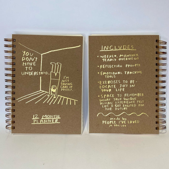 12 month planner notebook open flat; brown covers with yellow text and line-art, spiral binding